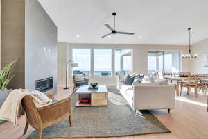 Living room featuring a fireplace, ceiling fan with notable chandelier, a water view, and light hardwood / wood-style flooring