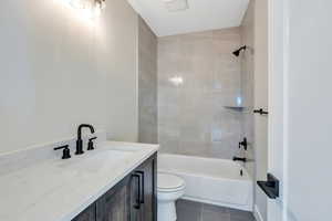 Full bathroom with toilet, tile patterned flooring, tiled shower / bath, and vanity