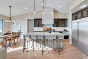 Kitchen with backsplash, a kitchen island with sink, dark brown cabinets, vaulted ceiling, and sink