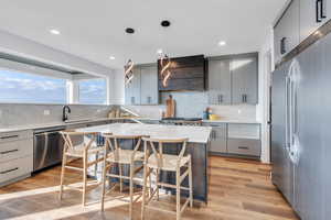 Kitchen with wall chimney range hood, gray cabinets, pendant lighting, a center island, and stainless steel appliances