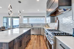 Kitchen featuring backsplash, premium range hood, high end range, pendant lighting, and sink