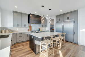 Kitchen featuring custom exhaust hood, gray cabinets, and built in fridge