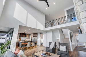 Living room with hardwood / wood-style flooring, ceiling fan, a barn door, and a towering ceiling