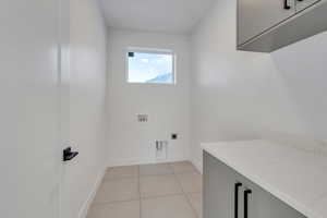 Laundry room featuring cabinets, light tile patterned floors, hookup for a washing machine, and electric dryer hookup