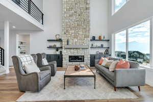 Living room with a fireplace, light wood-type flooring, plenty of natural light, and a towering ceiling