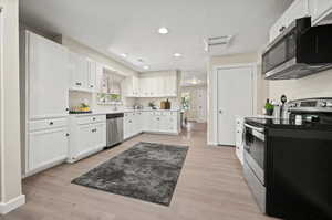 Kitchen with a textured ceiling, appliances with stainless steel finishes, light wood-type flooring, and white cabinetry