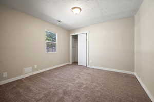 Unfurnished bedroom featuring carpet floors, a textured ceiling, and a closet