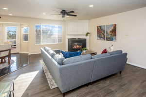 Living room with ceiling fan, dark wood-type flooring, and fireplace