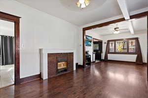 Finished living room featuring ceiling fan, dark hardwood flooring, a fireplace and beam ceiling