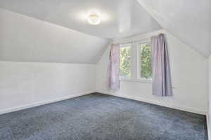 Bonus room featuring vaulted ceiling and dark carpet