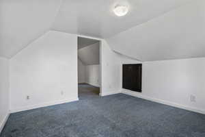 Bonus room with lofted ceiling and dark carpet