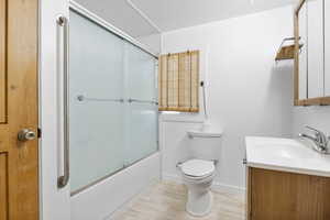 Full bathroom featuring shower / bath combination with glass door, vanity, toilet, and hardwood / wood-style flooring