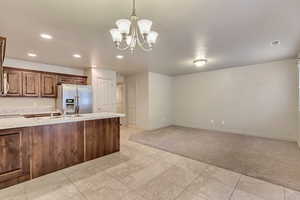 Kitchen featuring hanging light fixtures, sink, stainless steel fridge with ice dispenser, light carpet, and a notable chandelier