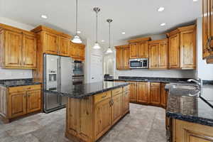 Kitchen with pendant lighting, sink, appliances with stainless steel finishes, a center island, and dark stone counters