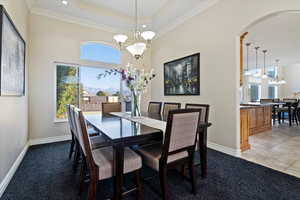 Dining space with carpet flooring, a chandelier, ornamental molding, and a wealth of natural light