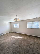 Carpeted spare room with a chandelier, a textured ceiling, and plenty of natural light