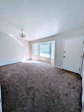 Unfurnished living room featuring a textured ceiling, carpet flooring, and an inviting chandelier