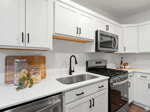 ADU Kitchen with appliances with stainless steel finishes, hardwood / wood-style floors, white cabinetry, and sink