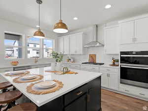 Kitchen featuring stainless steel appliances, hanging light fixtures, wall chimney range hood, and a center island