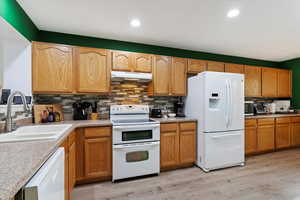 Kitchen with light hardwood / wood-style floors, sink, white appliances, and tasteful backsplash