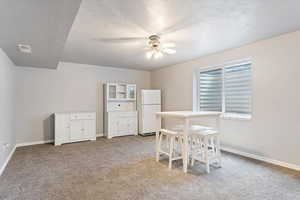 Interior space with a textured ceiling, ceiling fan, and light colored carpet