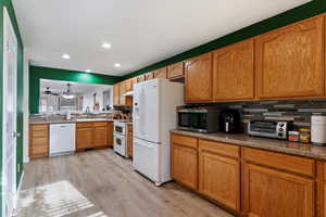 Kitchen with white appliances, backsplash, sink, and light wood-type flooring