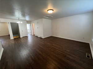 Empty room featuring an inviting chandelier and dark hardwood / wood-style flooring