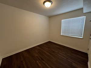 Empty room with dark hardwood / wood-style flooring and a textured ceiling