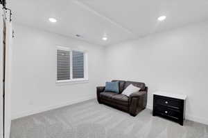 Living area with a barn door and light colored carpet