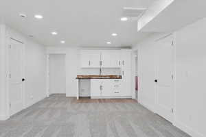 Interior space with white cabinetry, sink, and light colored carpet