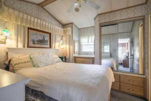 Bedroom with ceiling fan, dark colored carpet, and vaulted ceiling with beams