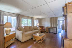 Living room with a paneled ceiling, dark hardwood / wood-style floors, wood walls, and a healthy amount of sunlight