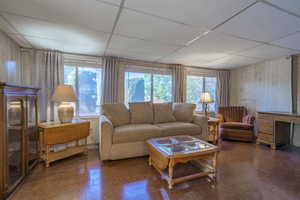 Living room with a paneled ceiling, wood walls, dark hardwood / wood-style floors, and a healthy amount of sunlight