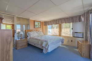 Carpeted bedroom featuring a drop ceiling, cooling unit, and wood walls