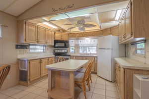 Kitchen featuring a kitchen island, white fridge, light tile patterned floors, and stainless steel electric range