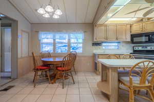 Kitchen with wood walls, electric range, an inviting chandelier, and light tile patterned floors