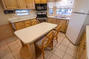 Kitchen featuring stainless steel range with electric stovetop, white fridge, light tile patterned floors, and sink