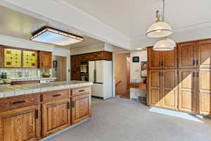 Kitchen featuring decorative backsplash, light carpet, pendant lighting, appliances with stainless steel finishes, and tile counters