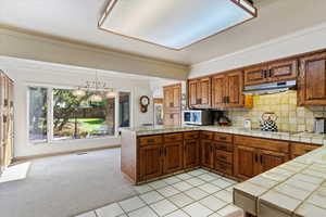 Kitchen featuring tile countertops, crown molding, hanging light fixtures, cooktop, and light tile patterned floors