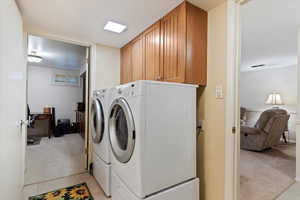 Laundry room featuring independent washer and dryer, light colored carpet, and cabinets