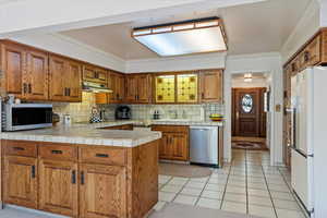 Kitchen featuring appliances with stainless steel finishes, kitchen peninsula, light tile patterned floors, and backsplash