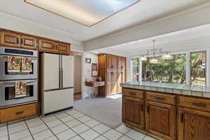 Kitchen with stainless steel double oven, light tile patterned flooring, crown molding, white refrigerator, and tile counters