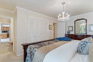 Carpeted bedroom featuring a notable chandelier, a closet, and ornamental molding