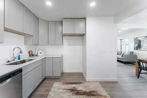 Kitchen with light hardwood / wood-style floors, gray cabinetry, sink, dishwasher, and a textured ceiling