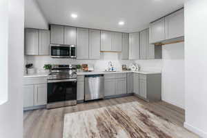 Kitchen with light hardwood / wood-style floors, gray cabinets, appliances with stainless steel finishes, and sink