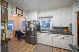 Kitchen with stainless steel refrigerator, white cabinets, and a healthy amount of sunlight