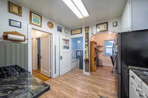 Kitchen featuring dark stone countertops, stainless steel refrigerator, light hardwood / wood-style flooring, and white cabinetry