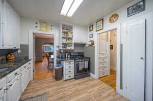 Kitchen featuring dark stone countertops, light wood-type flooring, gas stove, and white cabinetry