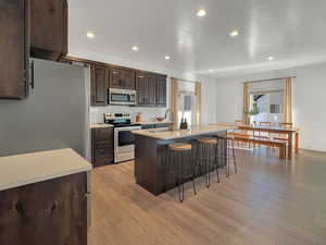 Kitchen with light hardwood / wood-style flooring, a center island with sink, sink, stainless steel appliances, and a textured ceiling