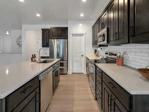 Kitchen featuring light wood-type flooring, sink, light stone countertops, an island with sink, and appliances with stainless steel finishes